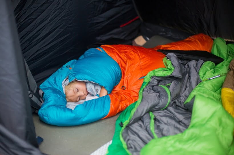 a child sleeping in camping tent and bag