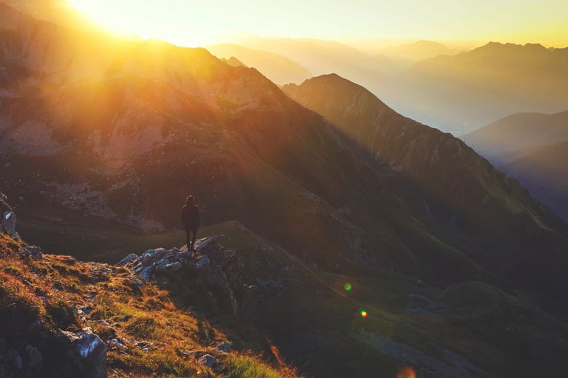 a person standing on a rock cliff and watching the golden hour