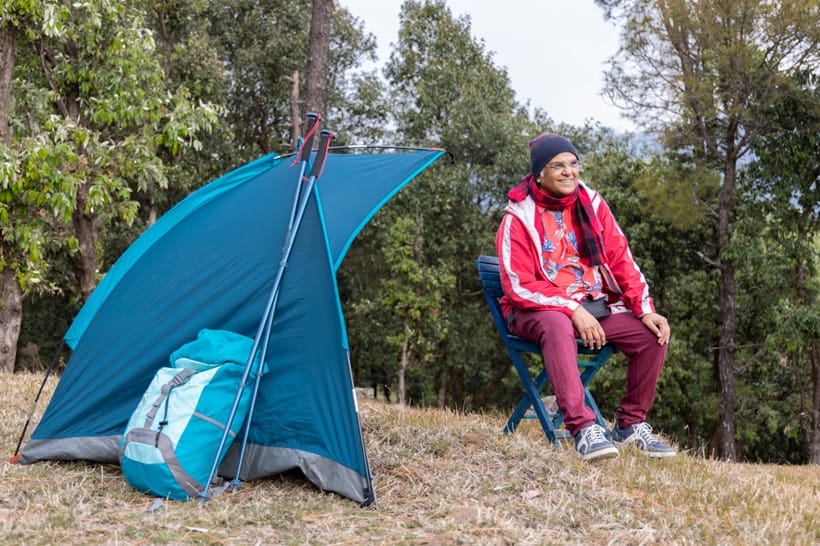an old man smiling in front of his tent