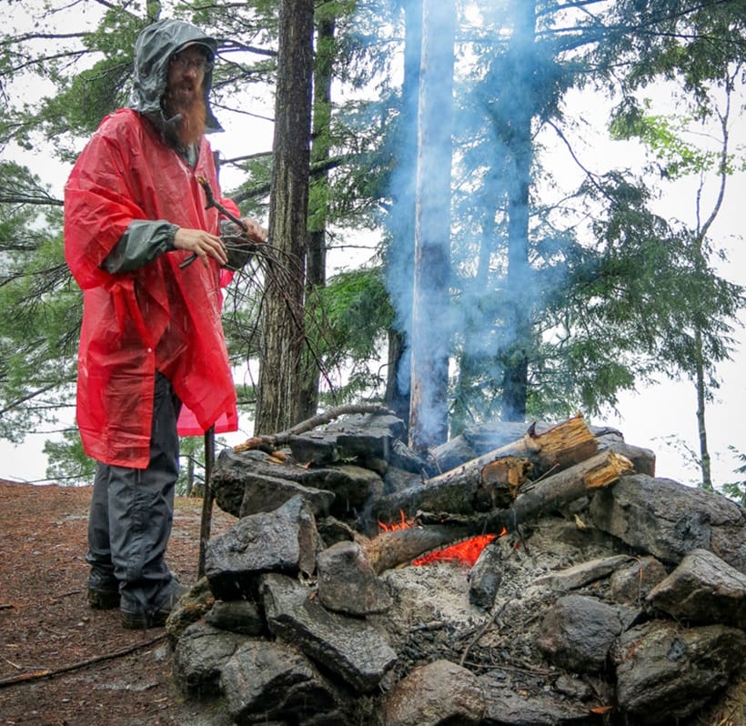 a camper standing next to fire in the rain