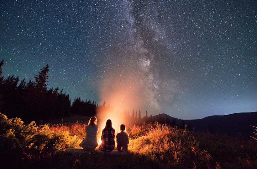 three women watching sky near campfire