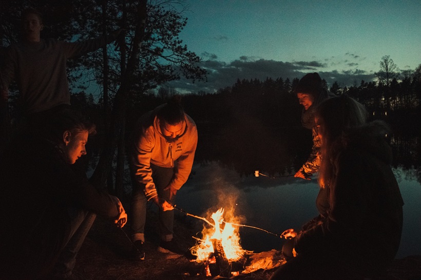 a group of friends making marshmallows around campfire